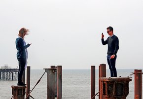 View of a man and a woman standing on the former west pier poles with the man taking photo of the woman. Photo by Alan Smallman.