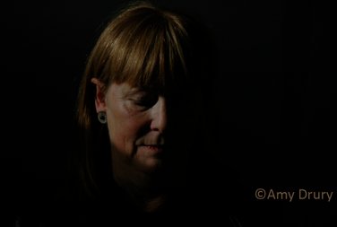 A low-key photo showing half the face of a female student who is looking downwards with closed eyes in full black background.Photo by Amy Drury.