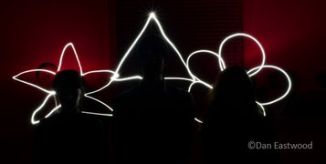Lightpainting photo by Dan Eastwood showing three silhouetted heads with halos in the shapes of two flowers in the edges and a triangle in the centre.