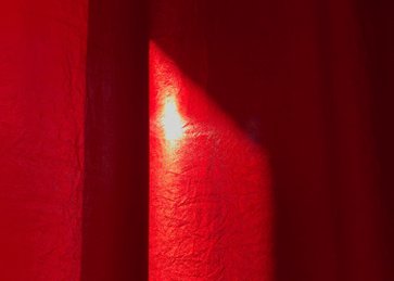 Κόκκινη κουρτίνα στην οποία ανακλάται το φως του ήλιου μέσα από τη σκιά του παραθύρου