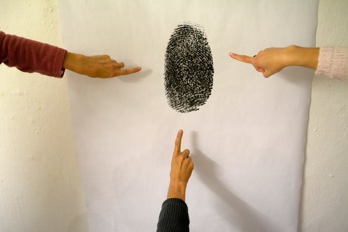 Picture of three fingers pointing to a photograph of an enlarged impression of an index finger in black ink..